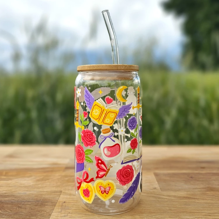 Szklany kubek 550 ml z bambusową pokrywką i szklaną słomką - smok siedzący na książce, wokół motywy z fantastyki i romansu - pocichutku.pl