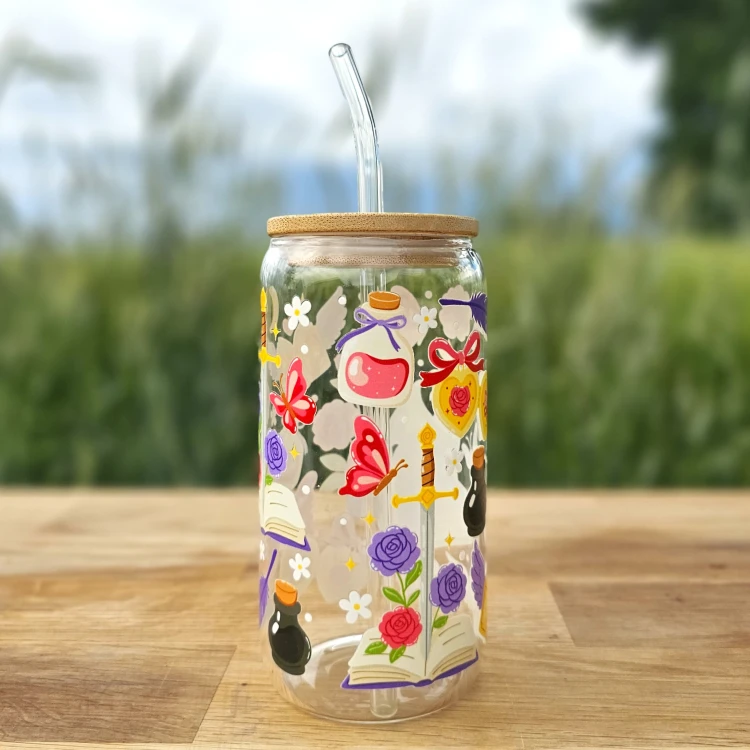Szklany kubek 550 ml z bambusową pokrywką i szklaną słomką - smok siedzący na książce, wokół motywy z fantastyki i romansu - pocichutku.pl