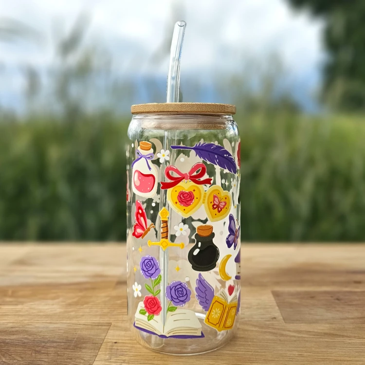 Szklany kubek 550 ml z bambusową pokrywką i szklaną słomką - smok siedzący na książce, wokół motywy z fantastyki i romansu - pocichutku.pl